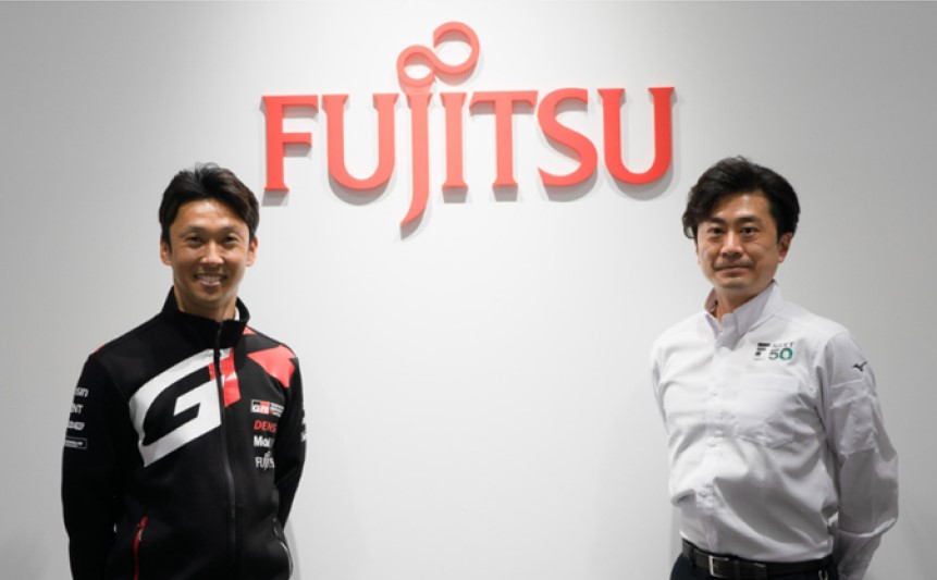 Dois homens a sorrir para a câmara em frente de uma parede com o logótipo da Fujitsu