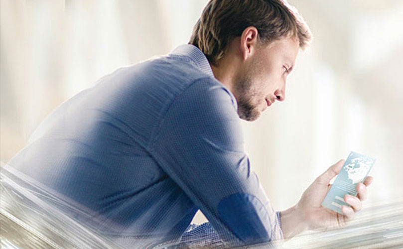 Side view of a man in a blue shirt, he intensely stares at his phone, displaying an image of the world. The background is blurred.