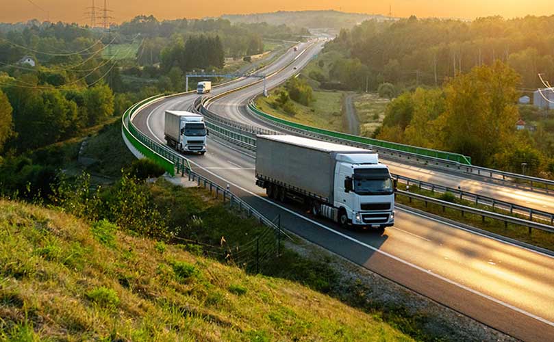 Flotte von LKW auf kurviger Autobahn bei Dämmerung