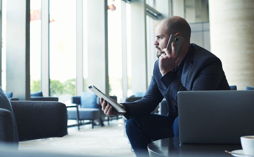 A man sitting on a chair holding a tablet and speaking on the phone