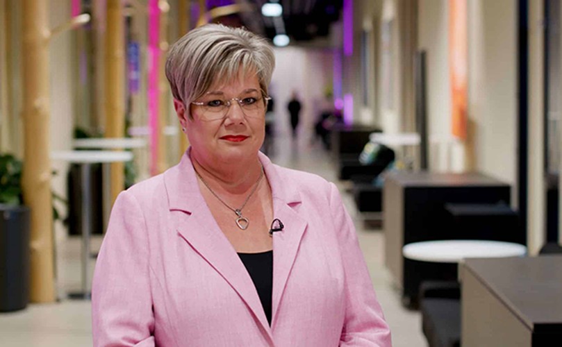 A woman in a pink suit stands confidently in a modern office setting, surrounded by contemporary furniture and decor.