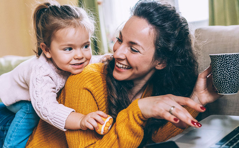 A woman and a child sit together on a couch, using a laptop for a shared activity.