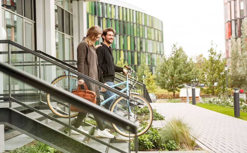 A man and woman leaving walking down a flight a stairs while holding a bycicle