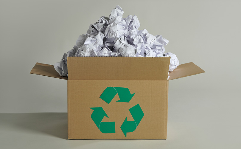 A cardboard box with a recycle symbol on it with ruffled paper stacked inside of it
