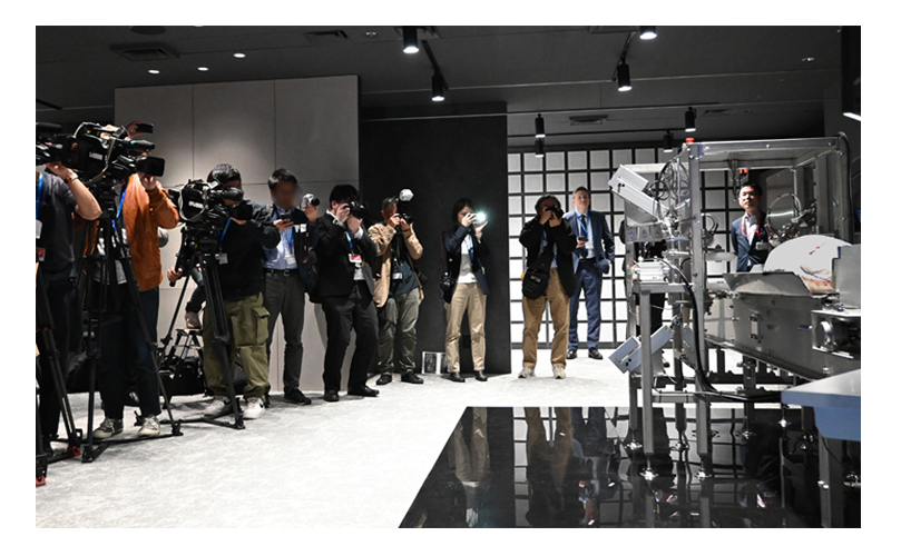 記者発表会で冷凍ビンチョウマグロの脂のりをAIで判定する「ソノファイT-01」を撮影するメディア(2025年4月 富士通本社)