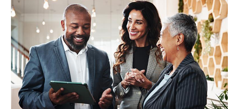 Three business people smiling and discussing something on a tablet.