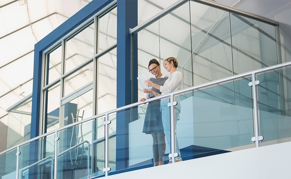 Two women review a tablet on a modern balcony.