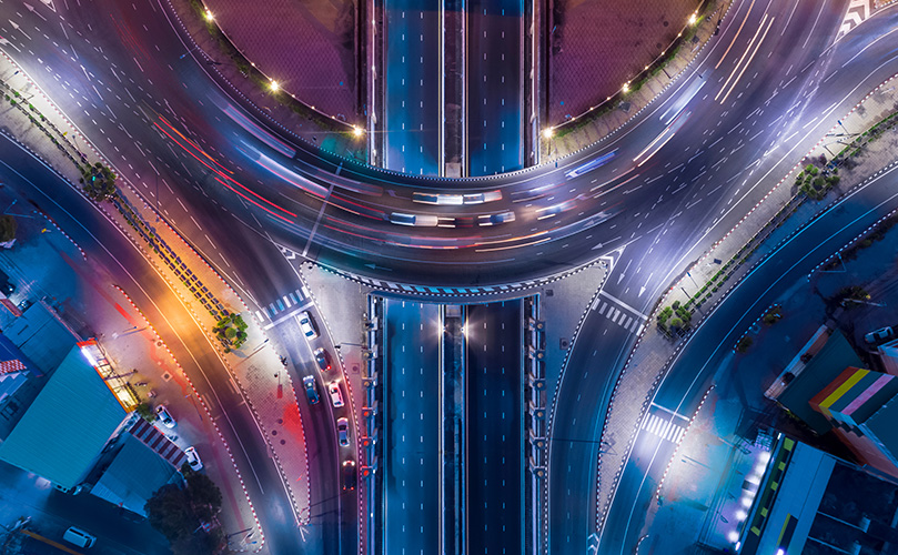 夜の高速道路のジャンクションを上から見た写真。車の光跡が残像のように写っている。