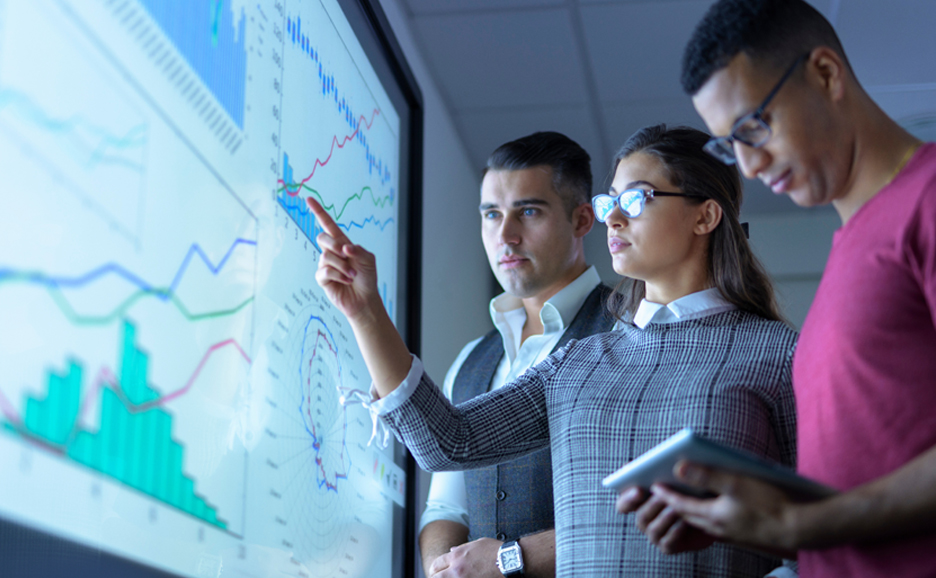 グラフが表示された画面を見ている3人のビジネスパーソン
