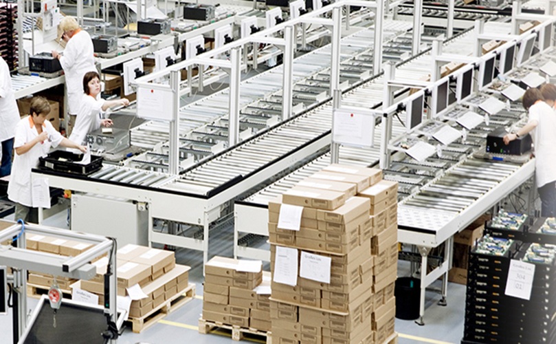 Inside a factory, multiple employees are actively working on the production floor, surrounded by machinery.