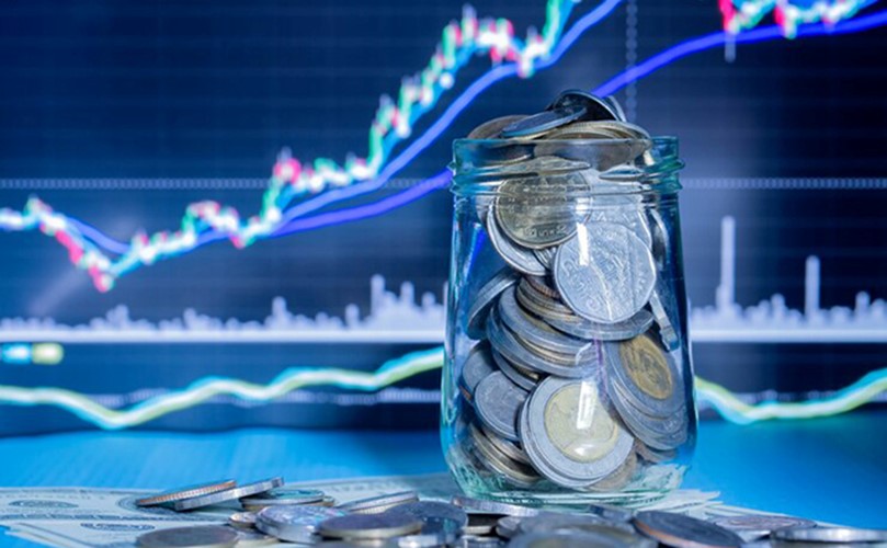 A money-filled jar is displayed with a stock market graph and coins in the background, representing financial growth.