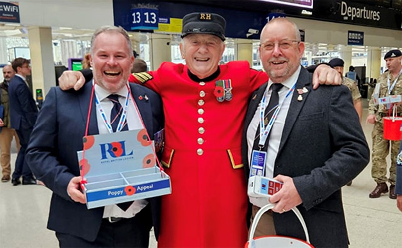 Three men dressed in red uniforms are carrying boxes, positioned closely together.
