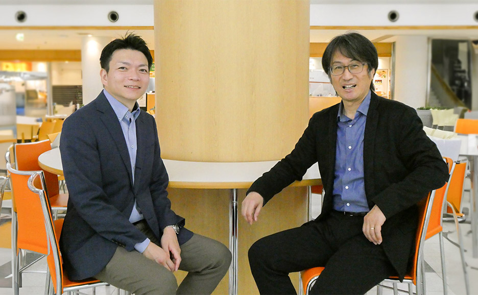 東洋大学社会学部長の桐生教授と、富士通の紺野が、大学の食堂で二人並んで座っている写真