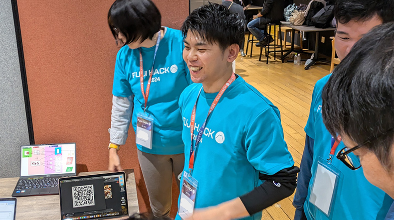 青いTシャツを着た参加者がチームで作り上げたデモを説明している写真