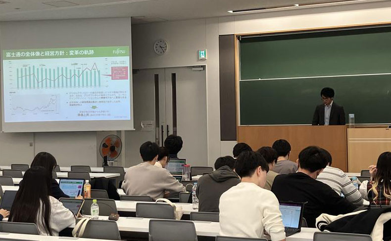 大学の教室で15名ほどの学生が、富士通社員から説明を受けている様子