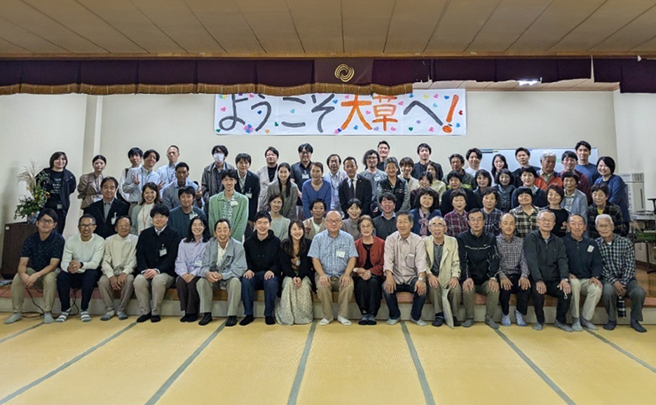 ようこそ大草へ！と書かれた横断幕の前で撮られている、50名ほどの集合写真