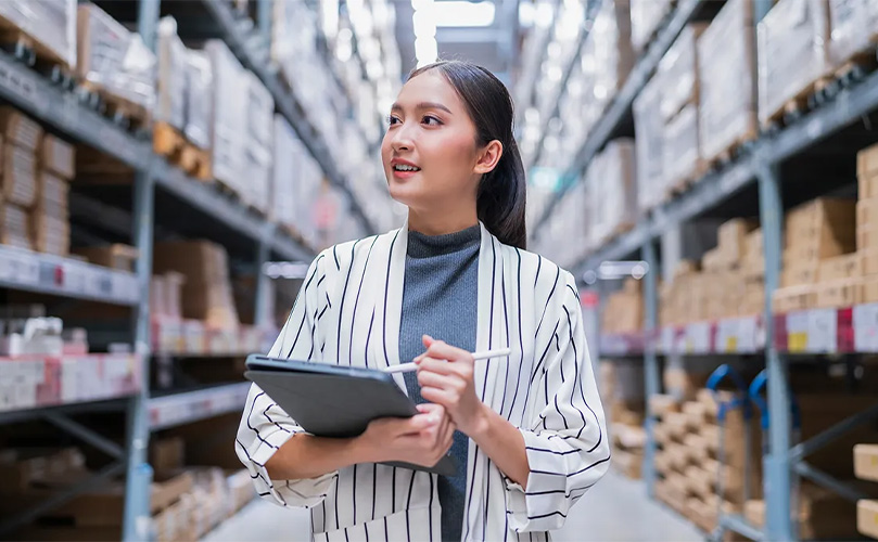 Junge asiatische Frau arbeitet mit einem digitalen Tablet in einem Logistiklager voller Kartons