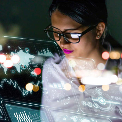 Eine Frau arbeitet vor transparent eingeblendeten digitalen Benutzeroberflächen mit Diagrammen und Datenvisualisierungen