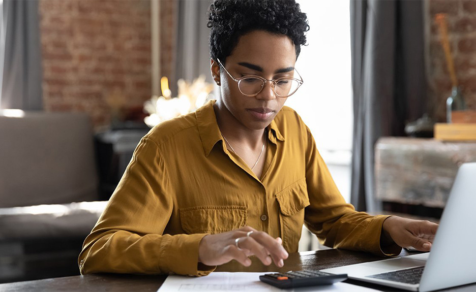 Geschäftsfrau arbeitet am Laptop und nutzt einen Taschenrechner am Schreibtisch.