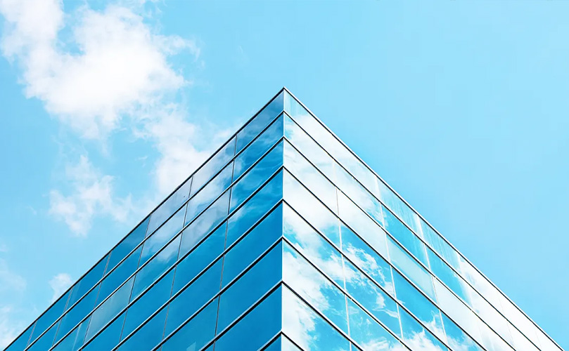 Nahaufnahme einer Ecke eines modernen Glasgebäudes, in dem sich der Himmel und die Wolken spiegeln