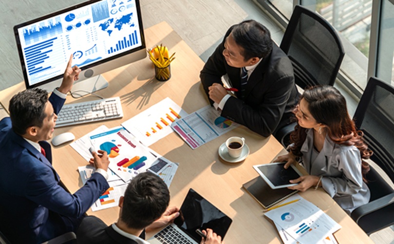A group of business people in a meeting room, collaborating with a laptop and documents spread across the table.