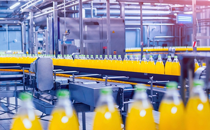 A conveyor belt transporting orange juice bottles in a production facility.