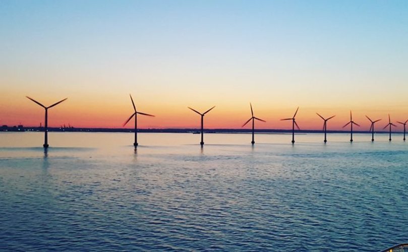 Wind turbines silhouetted against a vibrant sunset over the ocean, creating a serene and sustainable energy scene.