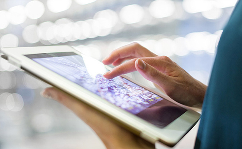 Close-up of a person’s hand using a touchscreen tablet, with a blurred background of white lights.