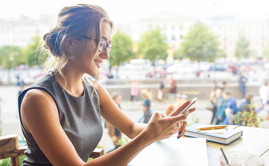 カフェでスマートフォンを見る笑顔の女性。