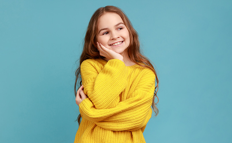 笑顔で頬杖をついている、黄色のセーターを着た若い女の子。