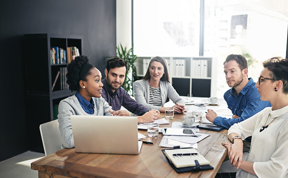 会議室でノートパソコンを囲んで話し合う5人のビジネスパーソン