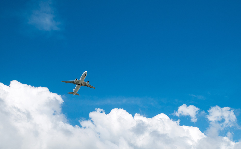白い飛行機が青空と白い雲の上を飛んでいる様子