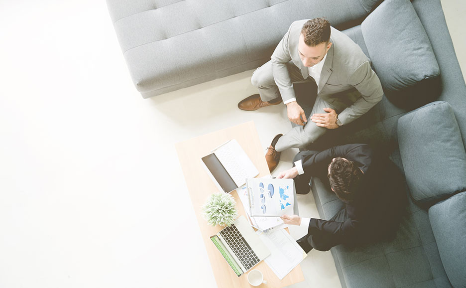 ビジネスウェアの男性2人がソファに座り、書類を見ています。