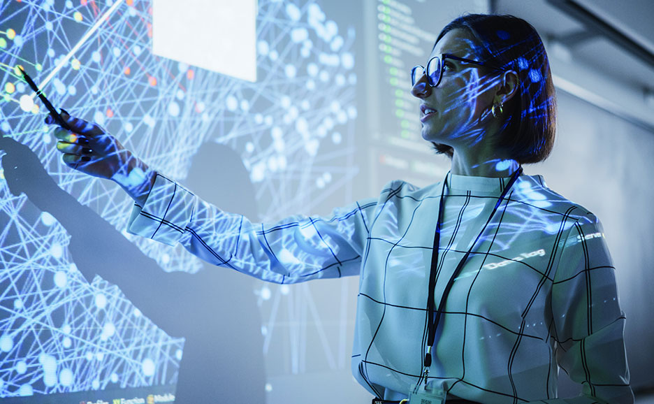 ネットワーク図を指し示す女性。顔やシャツに青い光が反射している。