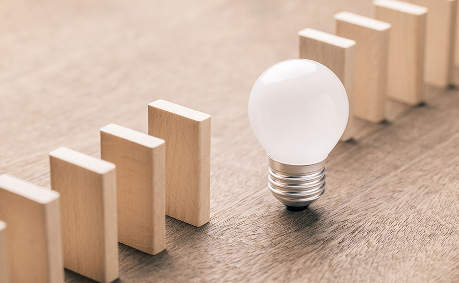 ドミノが並び、その中に電球一つを置いた、アイデアが問題を解決するイメージ。