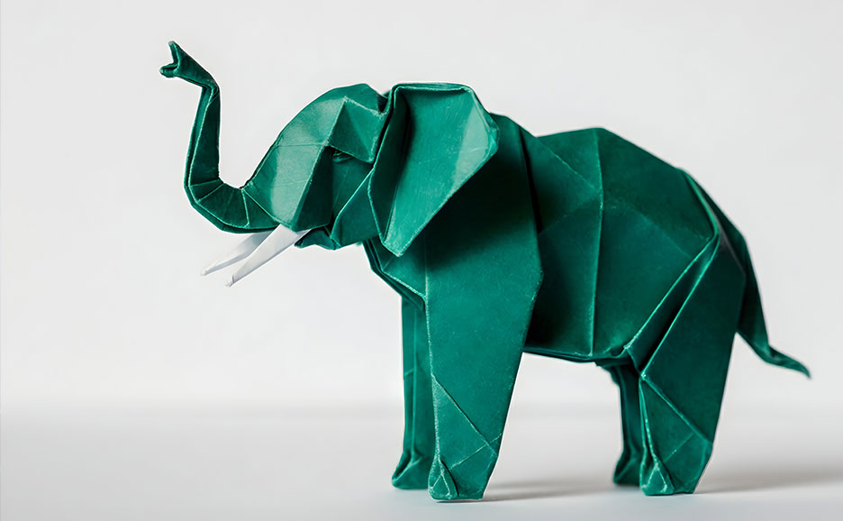 白い背景に、緑色の紙で折られた躍動感のある象の折り紙。