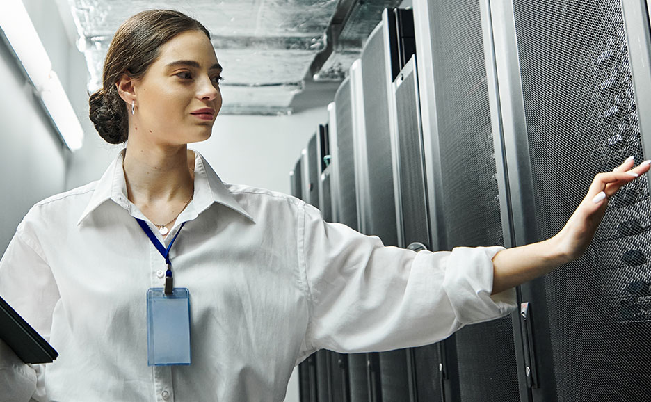 サーバルームでノートパソコンを持った女性がサーバのチェックをしている