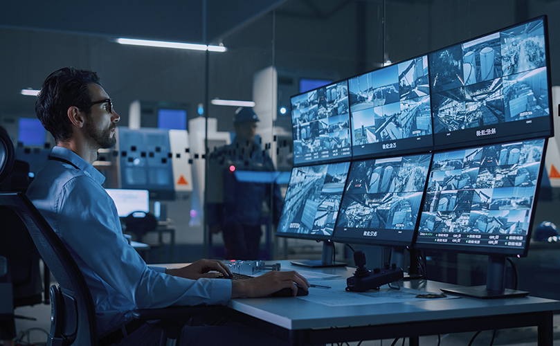 A man seated at a desk, focused on multiple computer monitors displaying various applications and data.