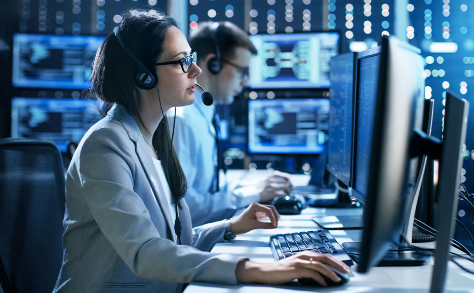 IT professionals monitoring systems on multiple screens in a control room