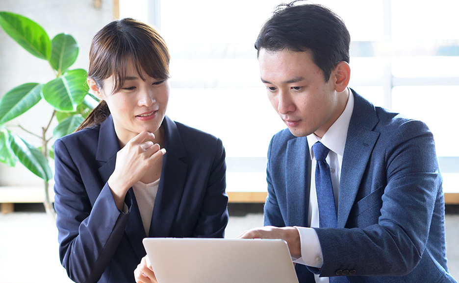 男女がノートパソコン画面を覗き込みながら真剣に話し合っている