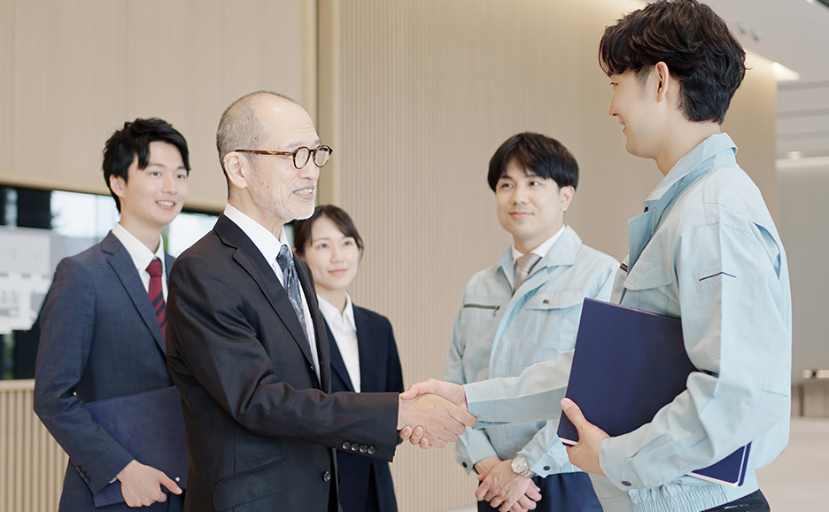 オフィスで握手を交わす二人とそれを見守るビジネスマン