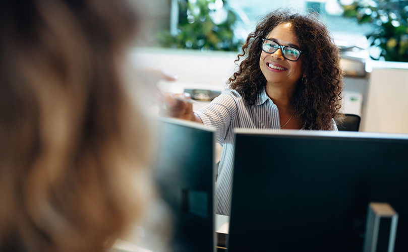 オフィスでパソコンに向かい、笑顔で誰かと話す女性。