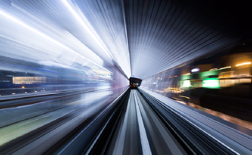 A train rushes through a tunnel, captured in a blurry image that conveys speed and movement.