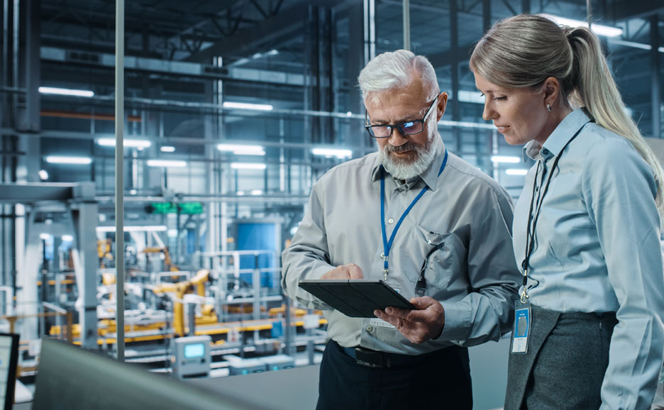 A man reviewing data and a woman following up in a manufacturing setting.