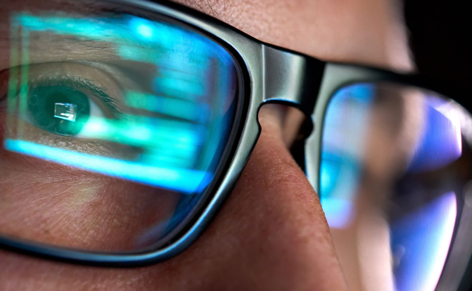 眼鏡をかけた人物の目に青いデジタル情報が反射している。