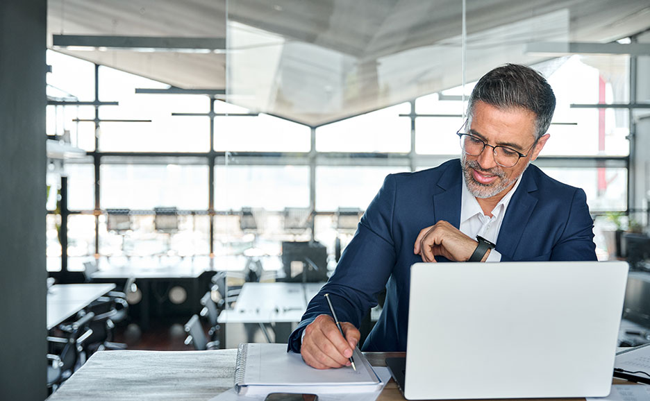 A man writing in a notebook while looking at a PC