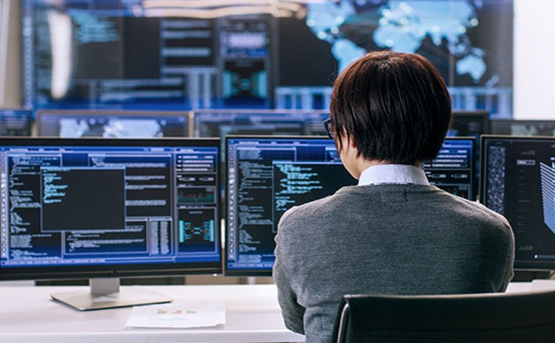 A woman seated at a desk, focused on multiple computer screens displaying various tasks and information.