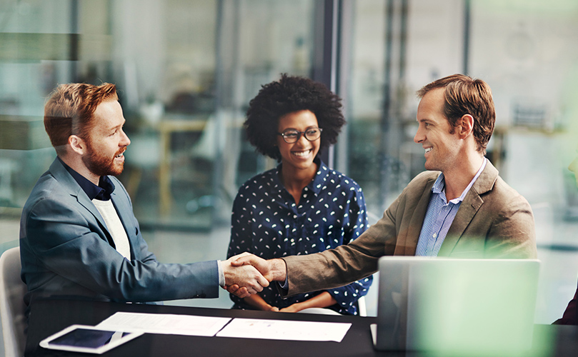  A group of diverse individuals shaking hands during a formal meeting, symbolizing collaboration and agreement.