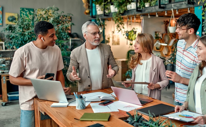 A group of diverse individuals gathered around a table, each using a laptop for collaboration and discussion.
