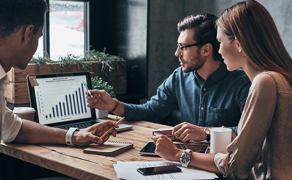 ラップトップのグラフを見ながら議論する3人のビジネスパーソン